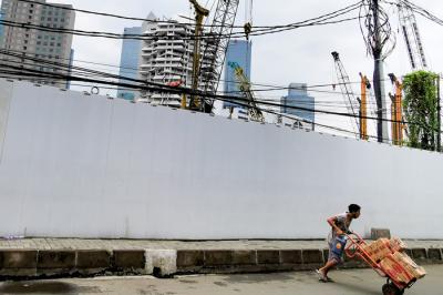 Warga melintasi proyek pembangunan gedung di Jakarta Pusat, Senin (5/4/2021).