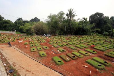 Petugas pemakaman menyiram rumput makam di TPU Jombang, Tangerang Selatan, Selasa (27/4/2021).