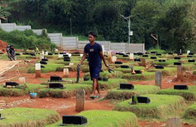 Petugas pemakaman menyiram rumput makam di TPU Jombang, Tangerang Selatan, Selasa (27/4/2021).