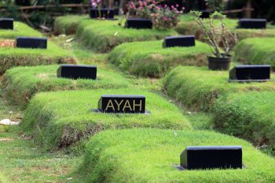 Petugas pemakaman menyiram rumput makam di TPU Jombang, Tangerang Selatan, Selasa (27/4/2021).
