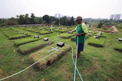 Petugas pemakaman menyiram rumput makam di TPU Jombang, Tangerang Selatan, Selasa (27/4/2021).