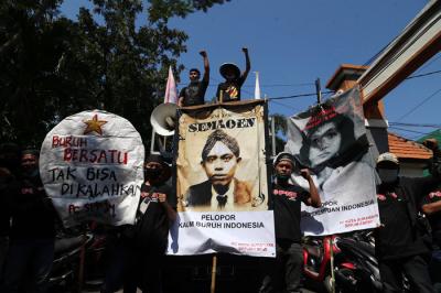Buruh membentangkan poster bergambar Semaoen dan Marsinah saat aksi May Day didepan kantor Disnakertrans Provinsi Jawa Timur, Sabtu (1/5/2021).