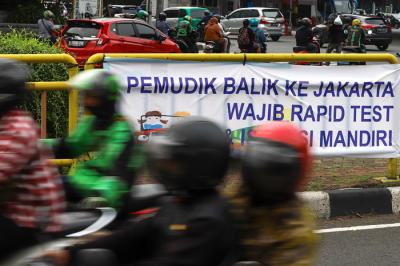 Pengendara melintasi spanduk bertuliskan himbauan kepada warga pemudik wajib test Covid-19 di Jakarta Barat, Senin (17/5/2021).
