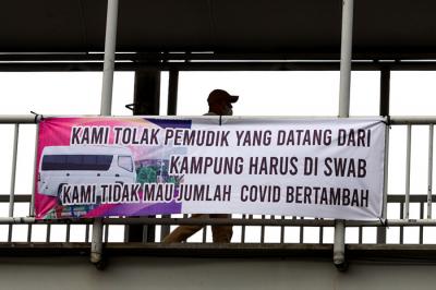 Pengendara melintasi spanduk bertuliskan himbauan kepada warga pemudik wajib test Covid-19 di Jakarta Barat, Senin (17/5/2021).