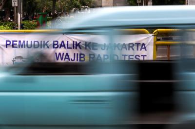 Pengendara melintasi spanduk bertuliskan himbauan kepada warga pemudik wajib test Covid-19 di Jakarta Barat, Senin (17/5/2021).