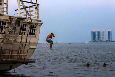 Sejumlah anak-anak asyik berenang di antara kapal-kapal yang bersandar di Pelabuhan Kaliadem, Muara Angke, Jakarta utara, Minggu (23/5/2021).