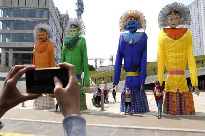 Pejalan kaki melintas di dekat pameran ondel-ondel berukuran rakasa di kawasan Taman Ismail Marzuki (TIM), Jakarta, Selasa (22/6/2021).