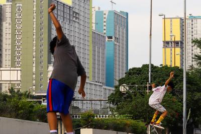 Anak-anak bermain skateboard dengan berlatar belakang gedung Rumah Sakit Darurat Covid-19 (RSDC) Wisma Atlet, Kemayoran, Jakarta Pusat, Selasa (22/6/2021).