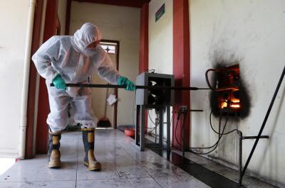 Petugas Krematorium mengenakan Hazmat dan APD memasukkan peti jenazah kedalam tungku pembakaran di Krematorium Keputih, Surabaya, Selasa (29/6/2021).