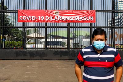 Warga melihat spanduk bertulis Covid-19 Dilarang Masuk terpasang di pagar kompleks DPR RI Jakarta, Jumat (9/7/2021).