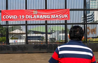 Warga melihat spanduk bertulis Covid-19 Dilarang Masuk terpasang di pagar kompleks DPR RI Jakarta, Jumat (9/7/2021).