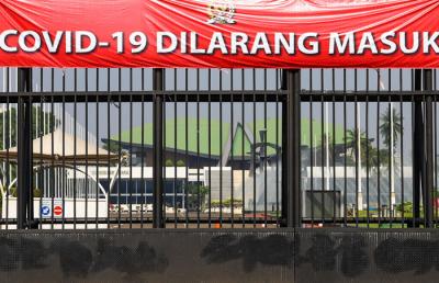 Warga melihat spanduk bertulis Covid-19 Dilarang Masuk terpasang di pagar kompleks DPR RI Jakarta, Jumat (9/7/2021).
