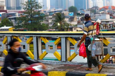 Pedagang kaki lima saat melintas di kawasan Tanah Abang dengan latar belakang pusat kota di Jakarta Pusat, Rabu (18/8/2021).