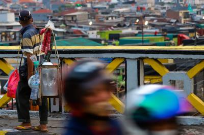 Pedagang kaki lima saat melintas di kawasan Tanah Abang dengan latar belakang pusat kota di Jakarta Pusat, Rabu (18/8/2021).