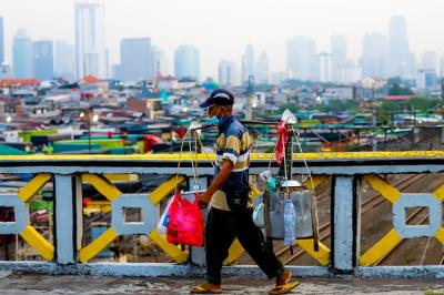 Pedagang kaki lima saat melintas di kawasan Tanah Abang dengan latar belakang pusat kota di Jakarta Pusat, Rabu (18/8/2021).