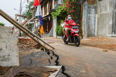 Warga melintas di Jalan Gudang Air yang mengalami keretakan di Kelurahan Rambutan, Kecamatan Ciracas, Jakarta Timur, Minggu (22/8/2021).