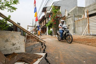 Warga melintas di Jalan Gudang Air yang mengalami keretakan di Kelurahan Rambutan, Kecamatan Ciracas, Jakarta Timur, Minggu (22/8/2021).