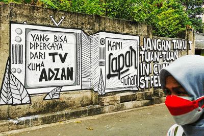 Warga saat melintas dengan berlatar belakang mural yang bertuliskan 'kami lapar tuhan' di Jakarta Pusat, Selasa (24/8/2021).