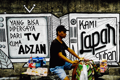Warga saat melintas dengan berlatar belakang mural yang bertuliskan 'kami lapar tuhan' di Jakarta Pusat, Selasa (24/8/2021).