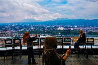 Pengunjung saat berfoto di atas gedung berlatar belakang pemandangan gunung dan awan di Bandung, Jawa Barat, Senin (25/10/2021).