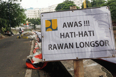 Warga melintas di samping jalan yang amblas di Jalan Inspeksi Kali Ciliwung, Jatinegara, Jakarta Timur.