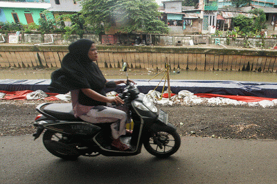 Warga melintas di samping jalan yang amblas di Jalan Inspeksi Kali Ciliwung, Jatinegara, Jakarta Timur.
