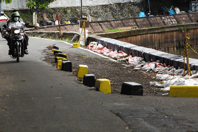 Warga melintas di samping jalan yang amblas di Jalan Inspeksi Kali Ciliwung, Jatinegara, Jakarta Timur.