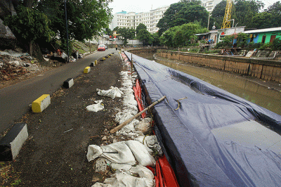 Warga melintas di samping jalan yang amblas di Jalan Inspeksi Kali Ciliwung, Jatinegara, Jakarta Timur.