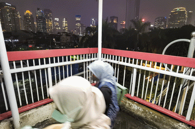 Pekerja melintas berlatar belakang gedung perkantoran di Jembatan Penyeberangan Orang, Jakarta, Senin (9/5/2022).