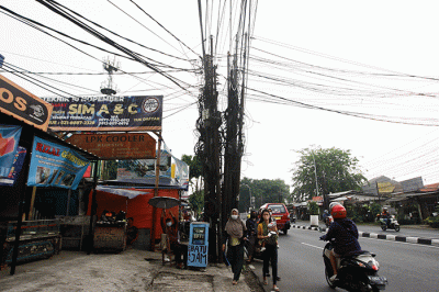 Warga melintas disamping instalasi kabel yang semrawut hingga menempel Jembatan Penyebrangan Orang (JPO) di kawasan Pasar Kramat Jati.