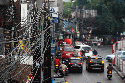 Warga melintas disamping instalasi kabel yang semrawut hingga menempel Jembatan Penyebrangan Orang (JPO) di kawasan Pasar Kramat Jati.