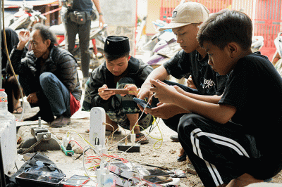 Sejumlah warga bergantian untuk mengisi daya ponselnya menggunakan genset keliling karena listrik masih padam imbas gempa bumi.