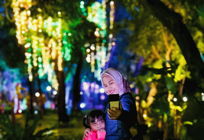 Pengunjung berfoto berlatar lampu warna-warni yang menerangi pepohonan di Taman Sumenep Jakarta Pusat, Kamis, (29/12/2022).