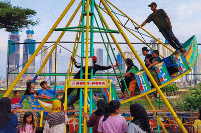 Warga asik bermain wahana Wisata rakyat murah meriah berlatar belakang gedung-gedung bertingkat di Taman Petamburan, Jakarta Pusat, Senin (2/1/2023).