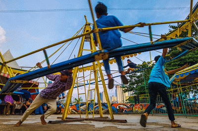 Warga asik bermain wahana Wisata rakyat murah meriah berlatar belakang gedung-gedung bertingkat di Taman Petamburan, Jakarta Pusat, Senin (2/1/2023).