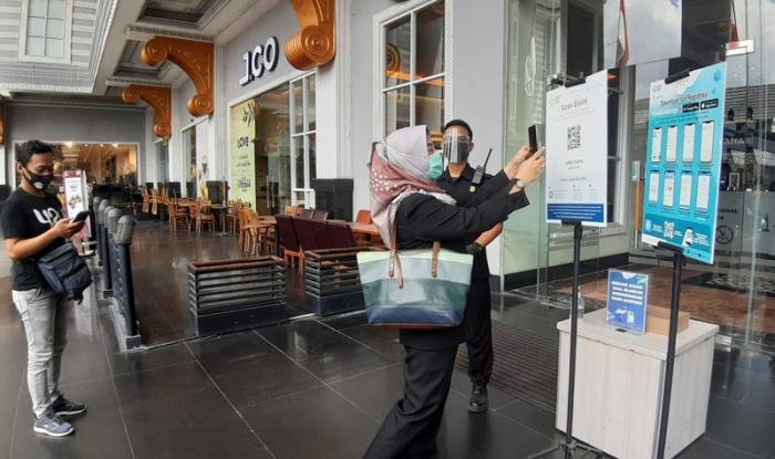 Pengunjung sedang scan barcode di aplikasi PeduliLindungi sebelum masuk mal