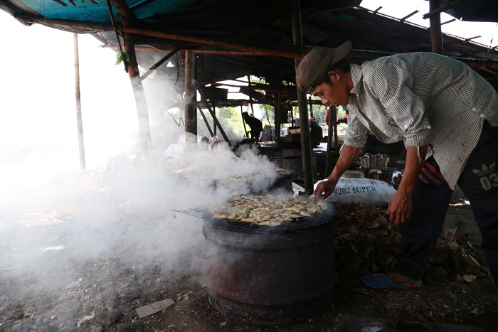 Perajin melakukan pengasapan ikan jenis patin di kawasan pesisir Kenjeran Surabaya, Jawa Timur, Kamis (18/3/2021).