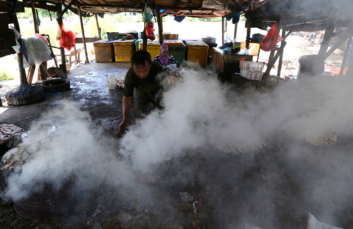 Perajin melakukan pengasapan ikan jenis patin di kawasan pesisir Kenjeran Surabaya, Jawa Timur, Kamis (18/3/2021).