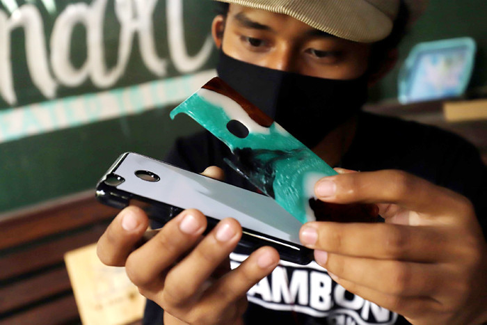 Perajin memasangkan casing atau pelindung telepon genggam dari bahan baku resin di Pondok Cabe, Tangerang Selatan, Banten, Rabu (31/3/2021).