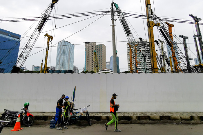 Warga melintasi proyek pembangunan gedung di Jakarta Pusat, Senin (5/4/2021).