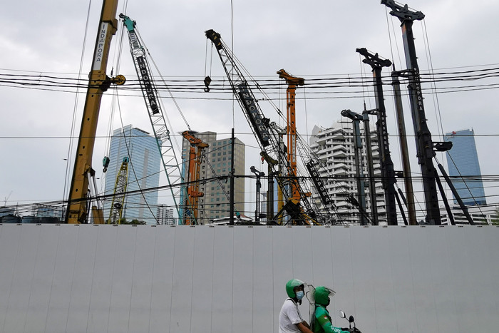 Warga melintasi proyek pembangunan gedung di Jakarta Pusat, Senin (5/4/2021).
