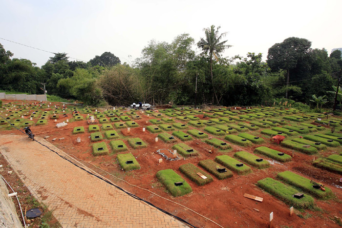 Petugas pemakaman menyiram rumput makam di TPU Jombang, Tangerang Selatan, Selasa (27/4/2021).