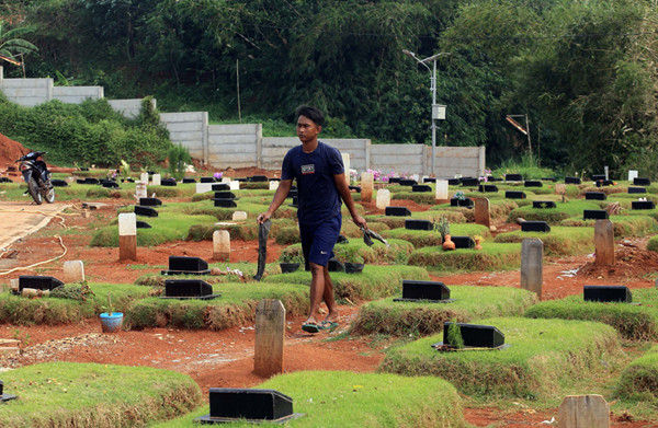 Petugas pemakaman menyiram rumput makam di TPU Jombang, Tangerang Selatan, Selasa (27/4/2021).