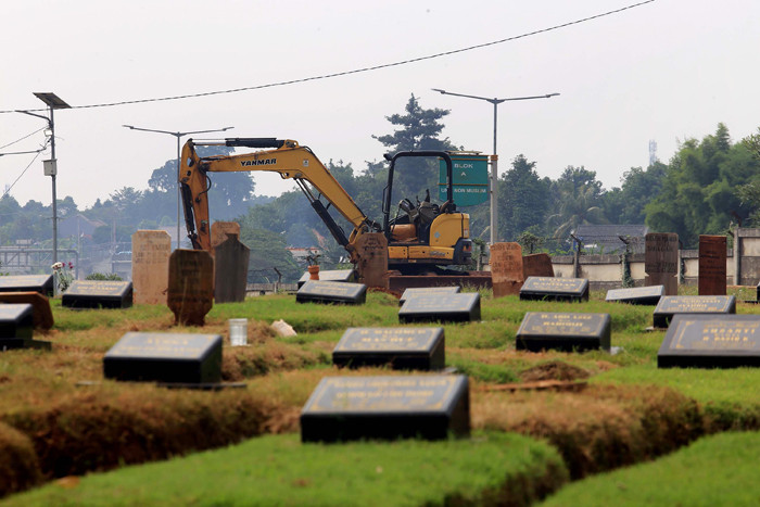 Petugas pemakaman menyiram rumput makam di TPU Jombang, Tangerang Selatan, Selasa (27/4/2021).