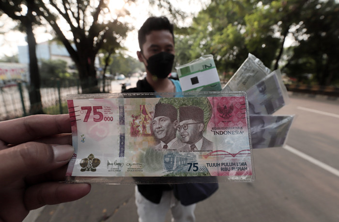 Penjual jasa penukaran uang menawarkan uang baru Rp75 ribu di kawasan Taman Mini Indonesia Indah, Jakarta Timur, Jumat (30/4/2021).