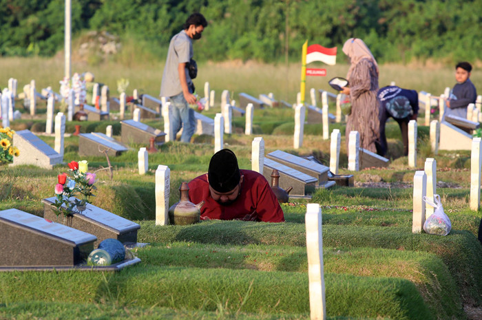 Kerabat korban Covid-19 membaca ayat-ayat suci Alquran dan berdoa ketika berziarah di makam khusus Covid-19, Keputih Surabaya, Jawa Timur, Rabu (12/5/2021).