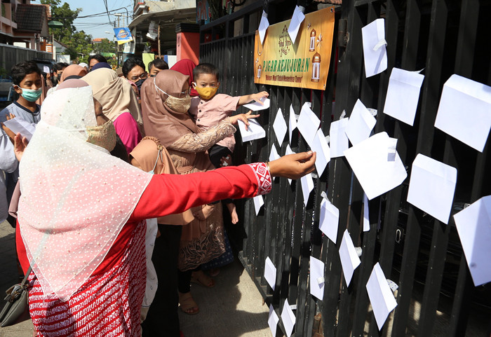Puluhan anak dan warga mengambil amplop lebaran di Pagar Kejujuran di kediaman keluarga Trisnadi Marjan di Sidoarjo, Jawa Timur, Kamis (13/5/2021).