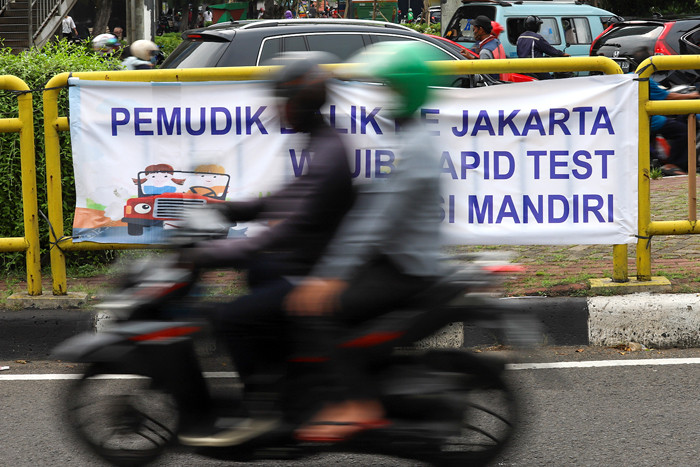 Pengendara melintasi spanduk bertuliskan himbauan kepada warga pemudik wajib test Covid-19 di Jakarta Barat, Senin (17/5/2021).