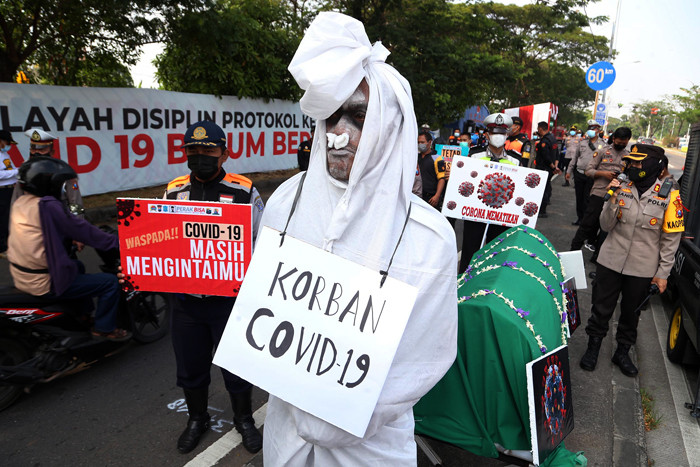 Sosok pocong korban Covid-19 jadi-jadian mengejutkan pengguna jalan saat melintas di pos penyekatan Polres Pelabuhan Tanjung Perak Surabaya, Sabtu (22/5/2021).