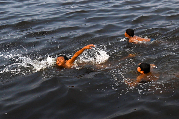 Sejumlah anak-anak asyik berenang di antara kapal-kapal yang bersandar di Pelabuhan Kaliadem, Muara Angke, Jakarta utara, Minggu (23/5/2021).